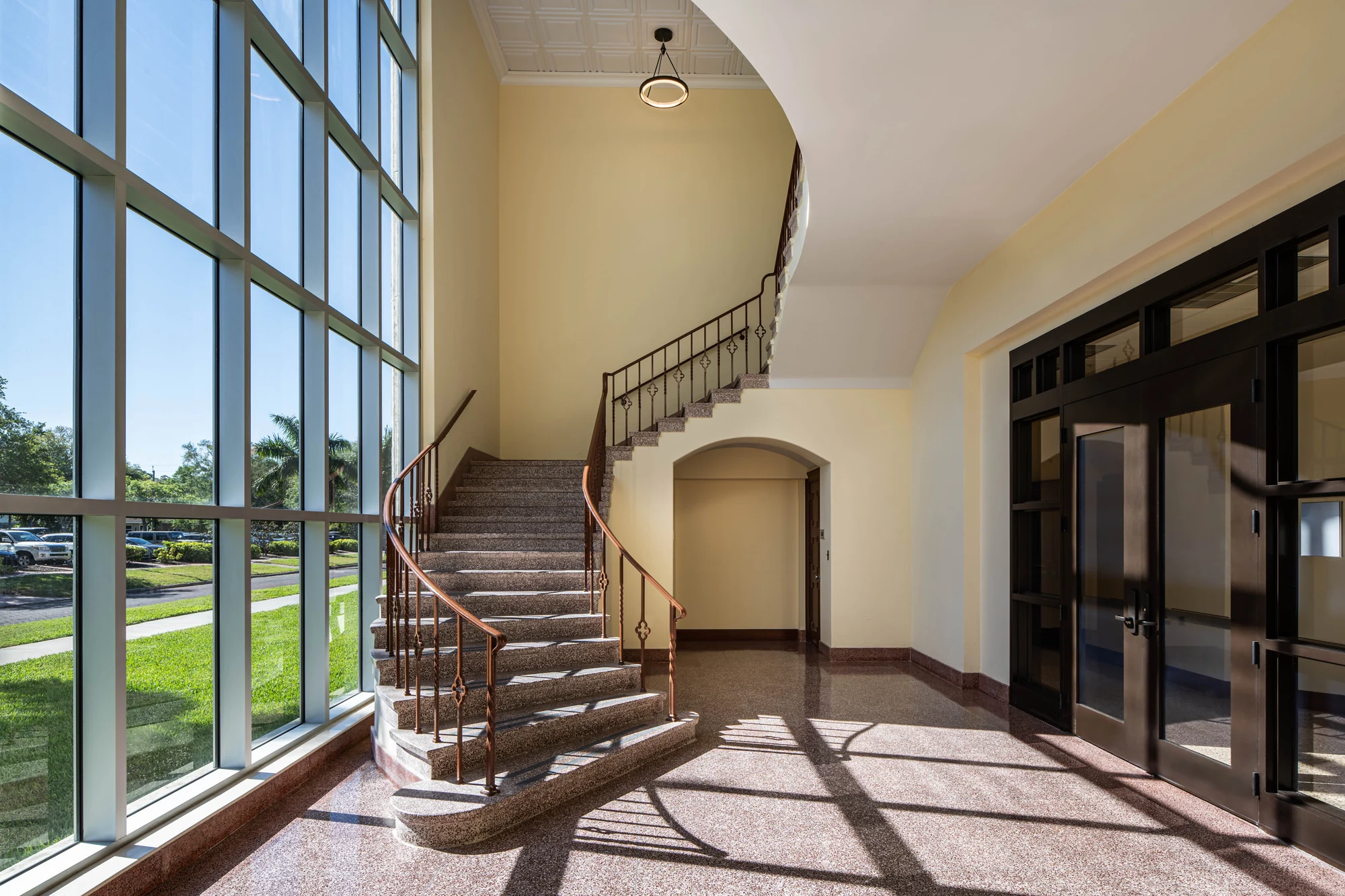 Curved staircase beside tall glazing with sunlight casting patterned shadows